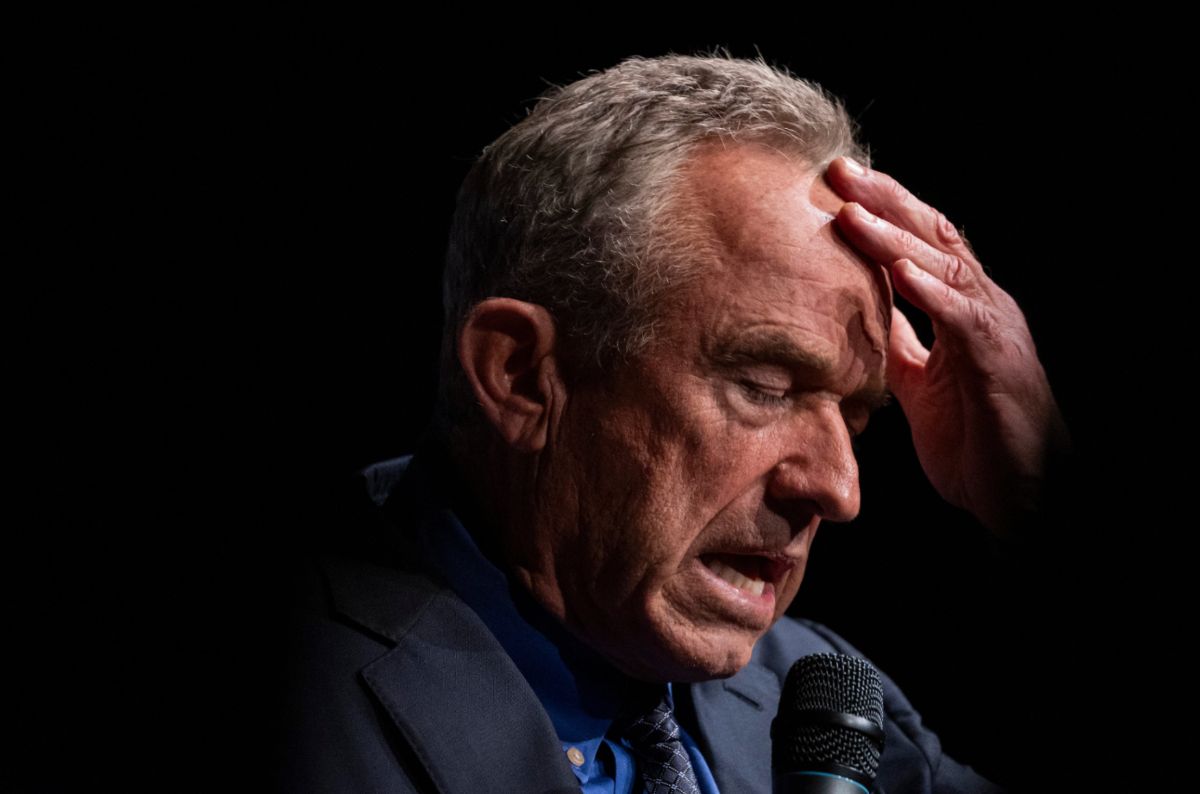 RFK Jr. speaking into a microphone with his hand on his forehead