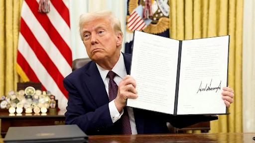 Donald Trump holds up a signed executive order in the Oval Office